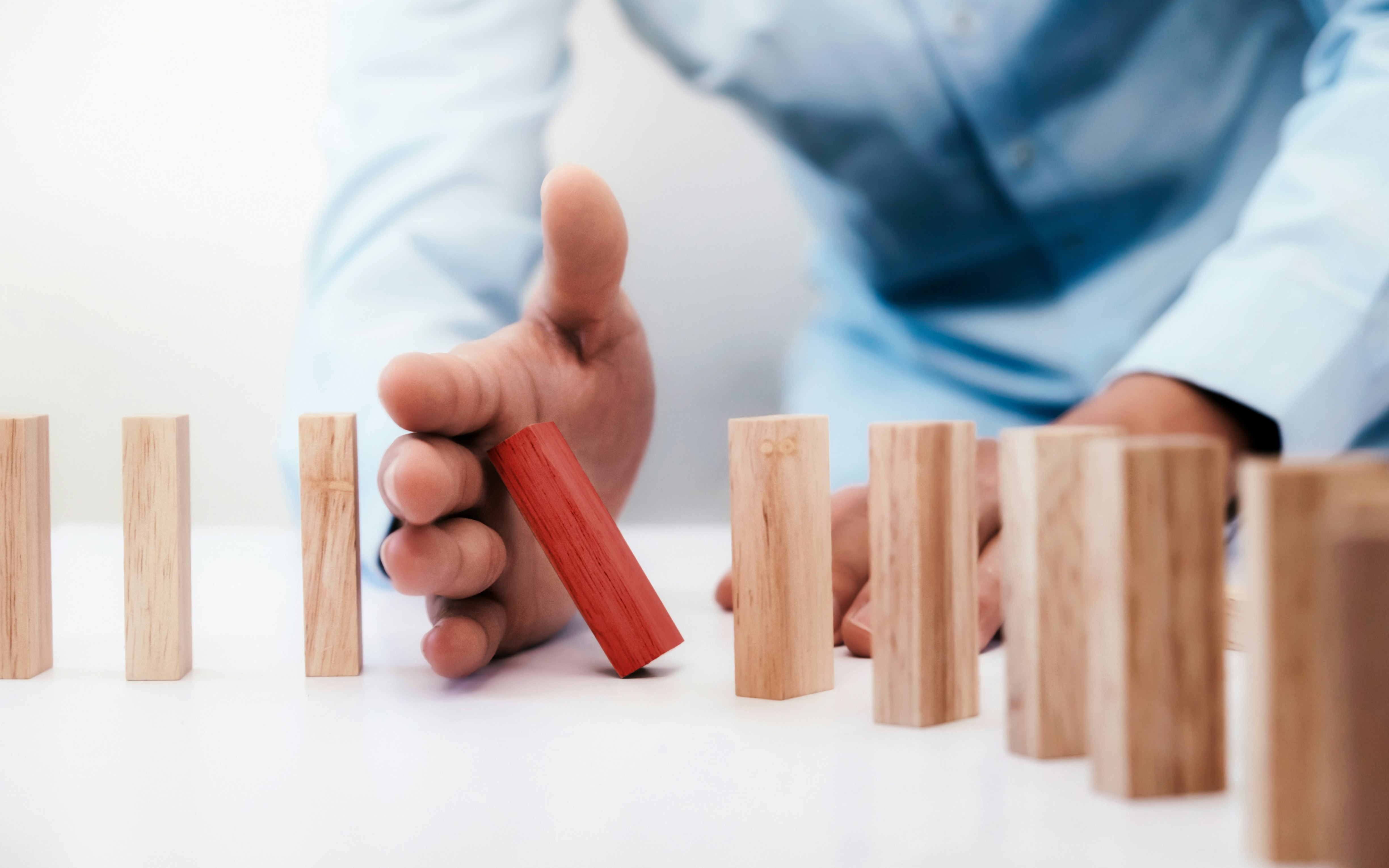 Businessman hand stop dominoes continuous toppled or risk with copyspace. Business risk, strategy and planing concept idea.