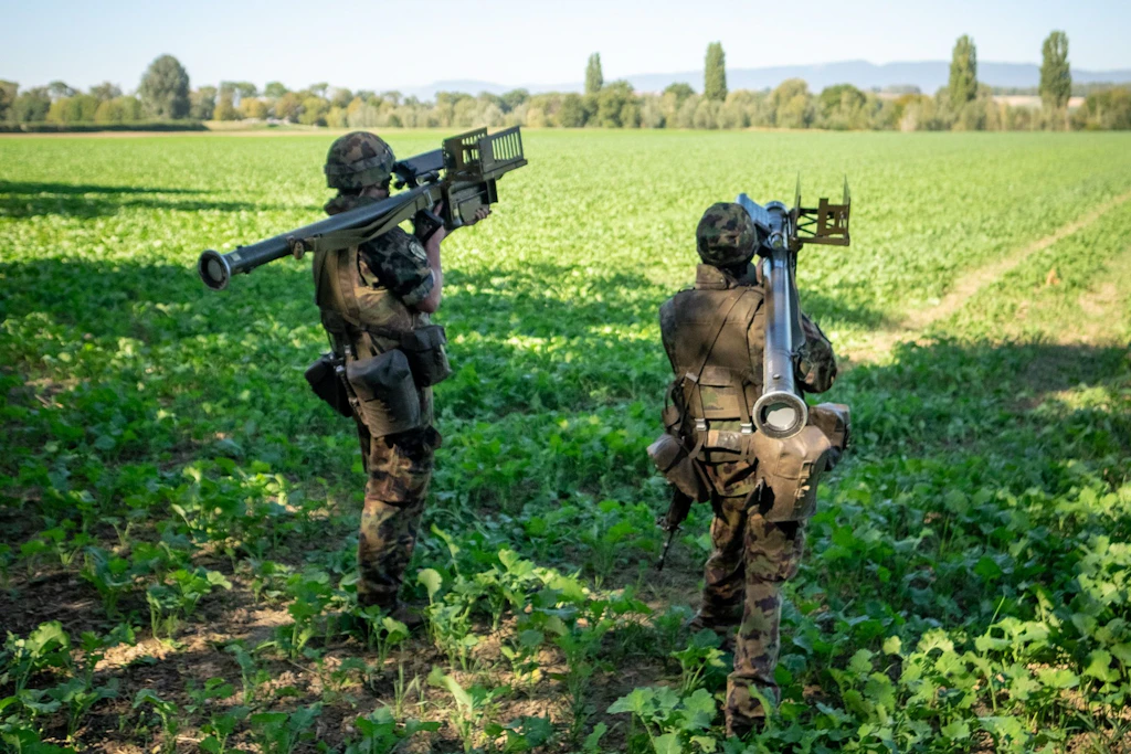 Zwei Soldaten stehen mit schultergestützten Stinger-Lenkwaffensystemen in einem Feld und beobachten den Luftraum.