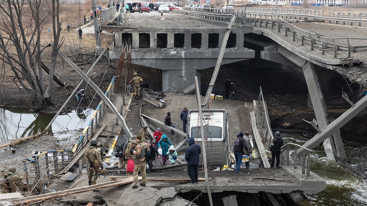 IRPIN, UKRAINE - Mar. 05, 2022: War in Ukraine. People cross a destroyed bridge as they evacuate the city of Irpin, northwest of Kyiv, during heavy shelling and bombing