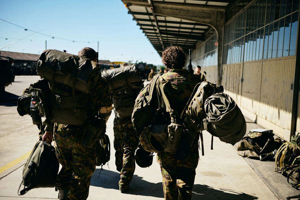 Trois militaires transportant un important équipement personnel traversent un site militaire.