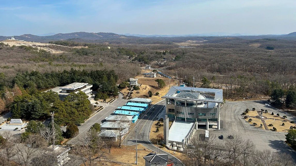 Vue aérienne de la zone de sécurité commune : au centre, on aperçoit les célèbres baraquements de conférence bleus, situés en plein milieu de la ligne de démarcation militaire entre la Corée du Nord et la Corée du Sud. À l’arrière-plan, on distingue le pont bleu qui mène au camp de la CSNN. 