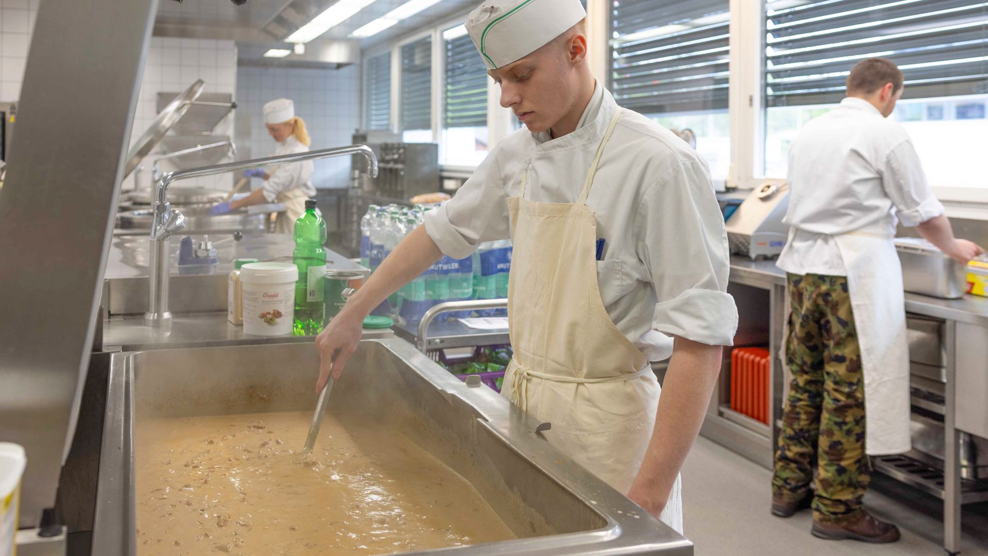 Da sinistra a destra: Joya Eicher, del secondo anno, prepara un contorno di verdure. Levi Ming, anche lui del secondo anno, lavora uno sminuzzato di vitello alla zurighese. Robin, cuoco di truppa in servizio aiuta gli apprendisti a preparare le ricette e si accerta, insieme al formatore professionale e all’altro cuoco, che il funzionamento della cucina si svolga nel rispetto delle regole di pulizia, igiene e puntualità.