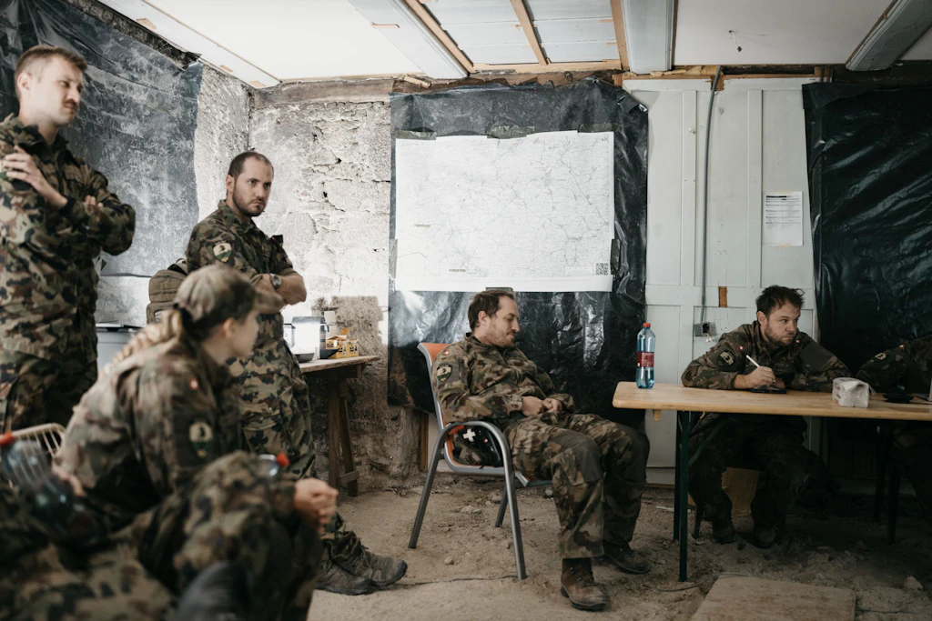 Diversi militari partecipano a una riunione in un locale allestito provvisoriamente; una grande carta è fissata alla parete.